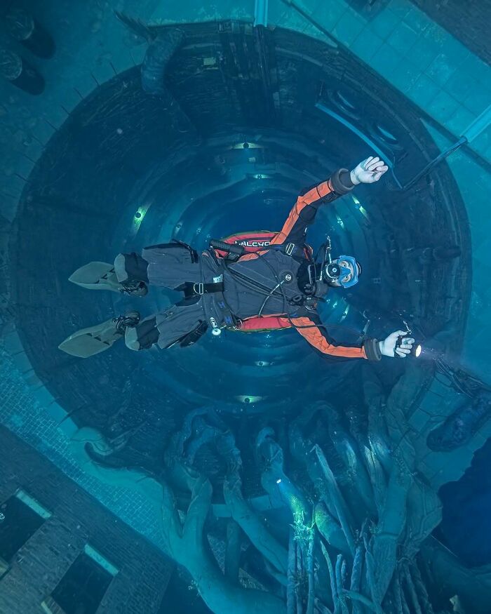 A diver explores deep uncomfortable water, making them feel small amidst the vast underwater structures and eerie lighting.