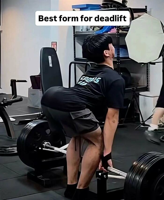 Man in black shirt performing a deadlift with improper form in a gym, highlighting a Darwin Award contender moment.