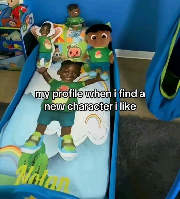 A toddler in a green shirt and shorts lays on a bed with Cocomelon dolls, a truly unhinged pic that makes no sense.