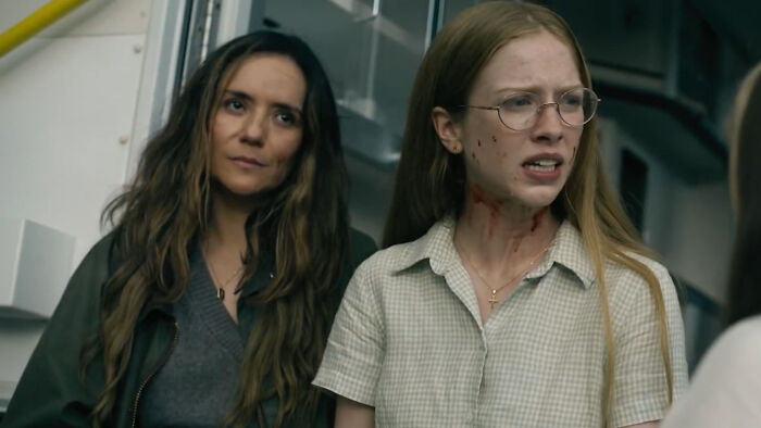 Duas mulheres da estreia da 4ª temporada, uma com óculos e sangue no pescoço, mostrando um momento tenso e aterrorizante.