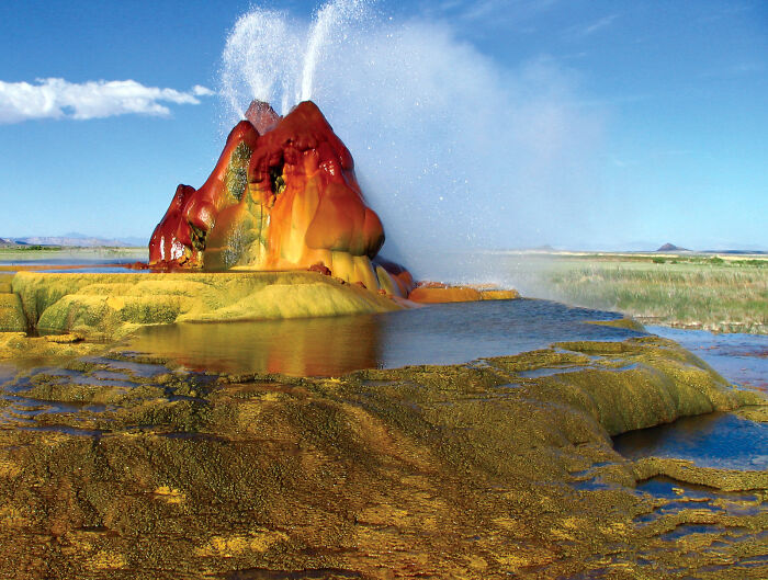 Unbelievable photos of Fly Geyser, a colorful geothermal cone, erupting water into a clear blue sky on Earth.