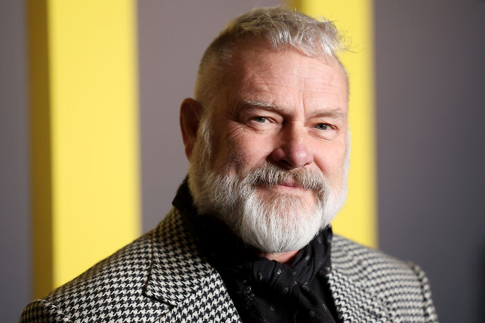 Homem barbudo com uma jaqueta estampada posando contra um fundo amarelo e cinza para a atualização da teoria do criador do Pitt, Dr. Robby.