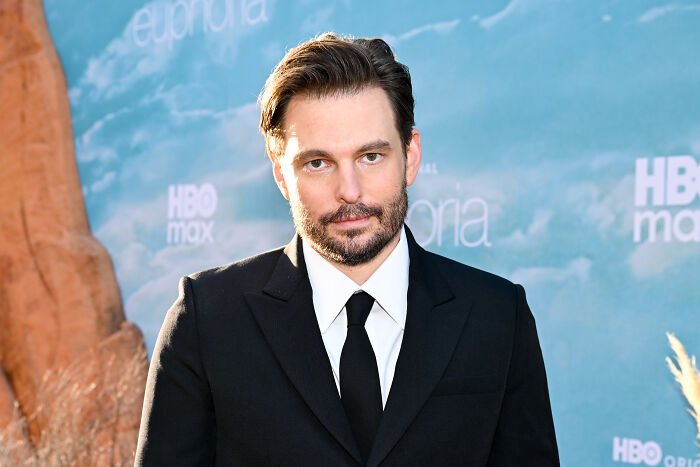 Homem de terno preto e gravata no evento de estreia da 3ª temporada de Euphoria, com os logotipos HBO Max e Euphoria ao fundo Homem de terno preto e gravata no evento de estreia da 3ª temporada de Euphoria, com os logotipos HBO Max e Euphoria ao fundo