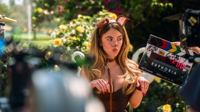 Sydney Sweeney, vestida com uma fantasia de cachorro com coleira, faz beicinho para a câmera. Uma ripa Euphoria é visível. Os fãs acham este vídeo do BTS desconfortável.