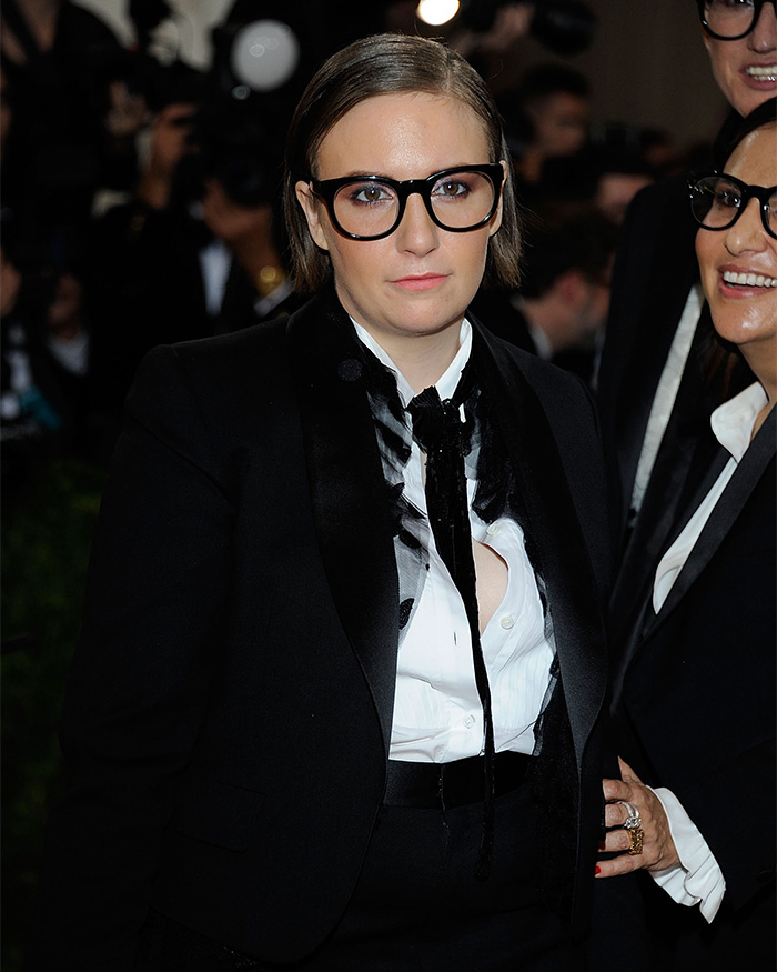 Lena Dunham in a black tuxedo jacket and white shirt, wearing glasses, at an event. Celebrities who hated the Met Gala.