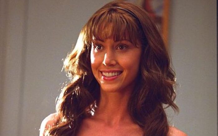 Uma mulher sorridente com cabelos castanhos e franja, uma paixão de infância, iluminada por trás, sugerindo um futuro brilhante em uma plataforma adulta.