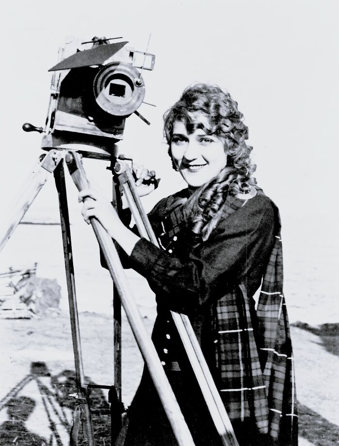Young woman operating an old vintage camera tripod in a rare and interesting photo from a time we will never experience again.