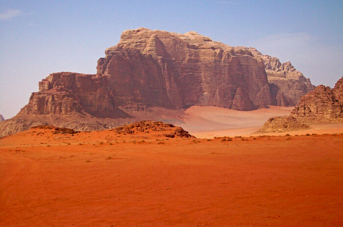 Unbelievable Photos Taken On Earth, showing a vast red desert landscape with towering rock formations under a clear sky.