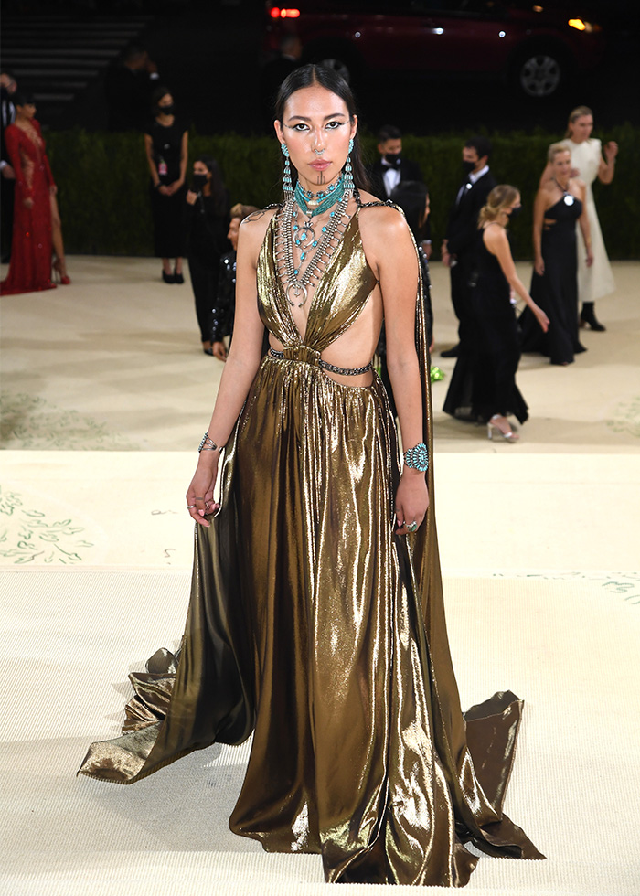 Quannah Chasinghorse at the Met Gala, wearing a golden gown and intricate turquoise and silver jewelry. Celebrities at the Met Gala.