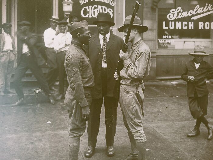 Two soldiers and a man in a suit talking outside a lunchroom in a rare and interesting historical photo.
