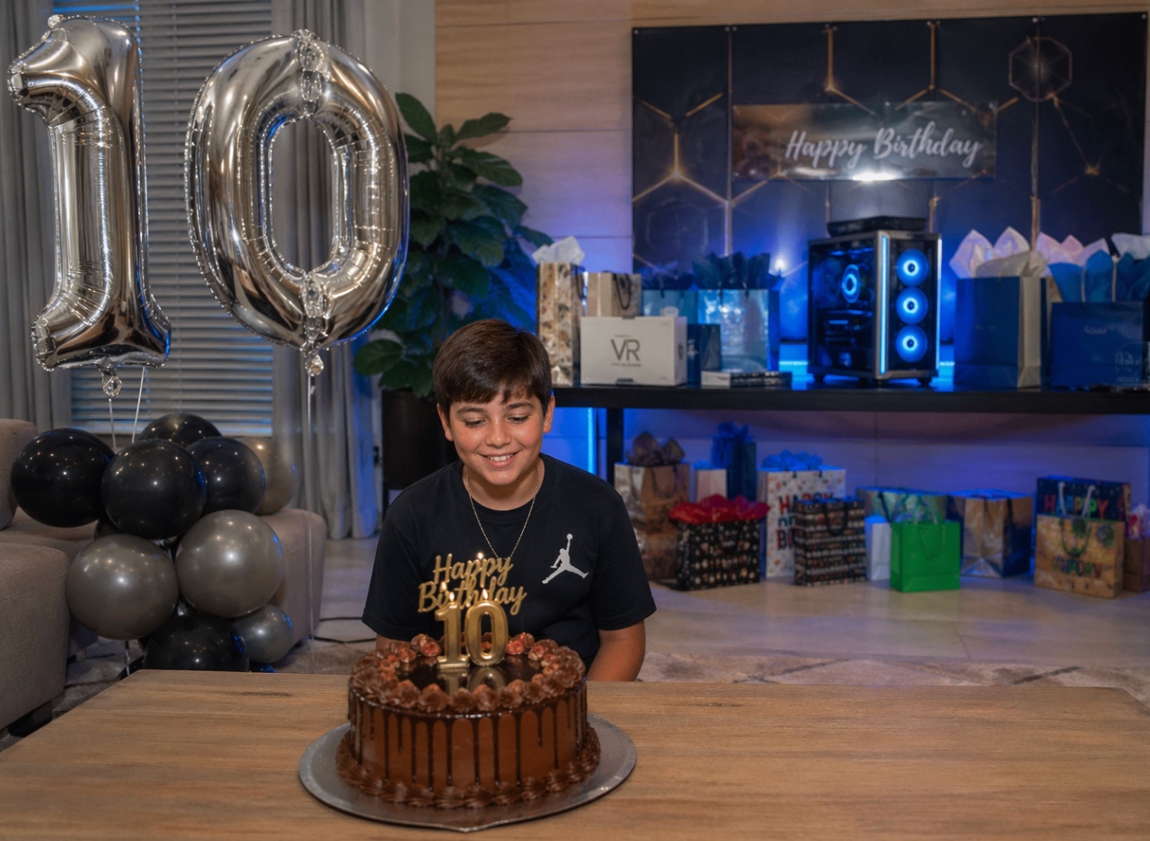 Boy celebrating 10th birthday with chocolate cake and balloons in a decorated room for Daily Dice Of Drama event.