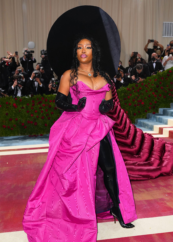 SZA on the Met Gala red carpet, wearing a striking hot pink gown, black gloves, and an enormous black hat. Many celebrities hated the Met Gala.