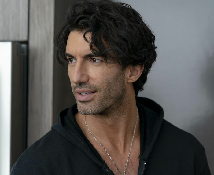 Man with dark wavy hair and stubble wearing a black hoodie, reacting to Blake Lively lawsuit against Justin Baldoni dismissal news.