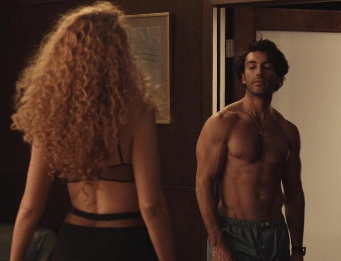 Man with muscular build facing woman with curly hair in dimly lit room, reflecting tension in Blake Lively lawsuit news reaction.
