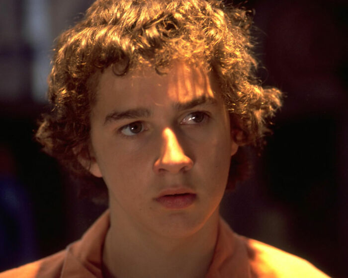 Young man with curly hair in dramatic lighting, reflecting the controversial remarks by Bryan Cranston on Shia LaBeouf.