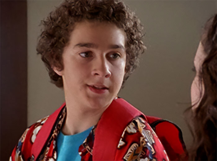 Young man with curly hair wearing a red backpack and patterned shirt capturing Bryan Cranston’s remarks on Shia LaBeouf.
