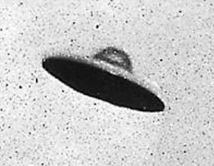 Grainy black and white photo of a dark, classic flying saucer UFO against a speckled sky, one of many mysterious things.