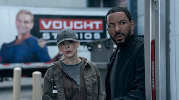 Two characters from The Boys Season 5 looking alert near a truck with Vought Studios logo in the background.