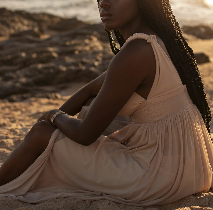 Woman with long braids sitting on sandy beach at sunset reflecting on urban legends that were unexpectedly true.