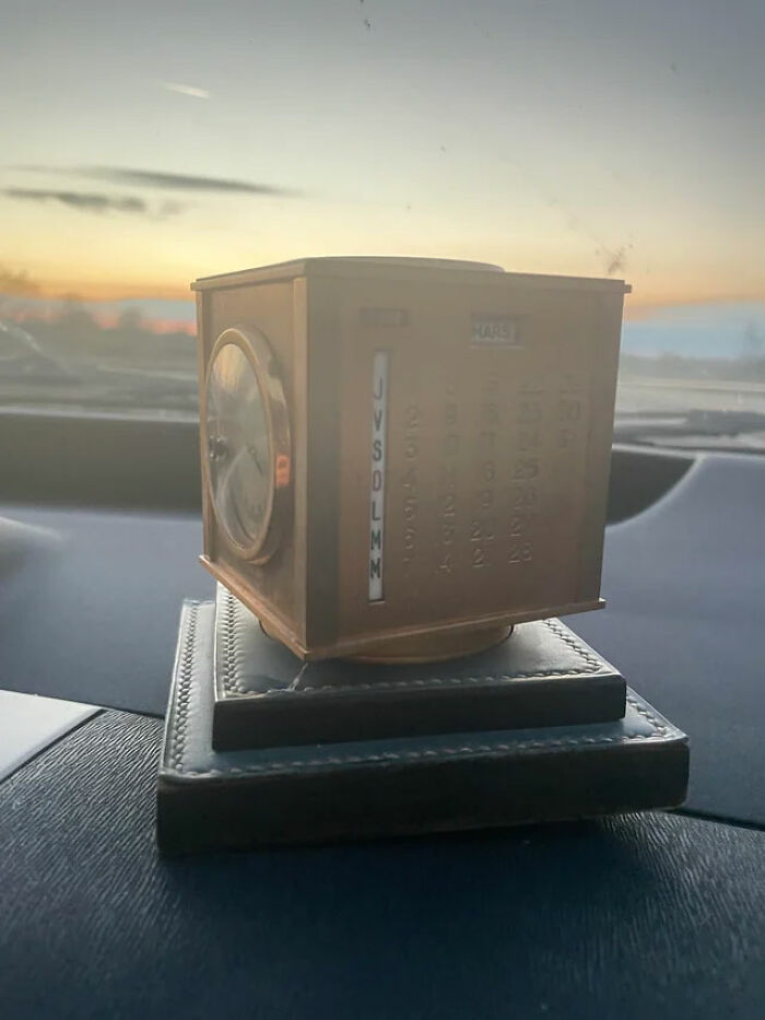 A unique bronze perpetual calendar and clock, an unusual possession, sits on a dashboard with a beautiful sunset in the background.