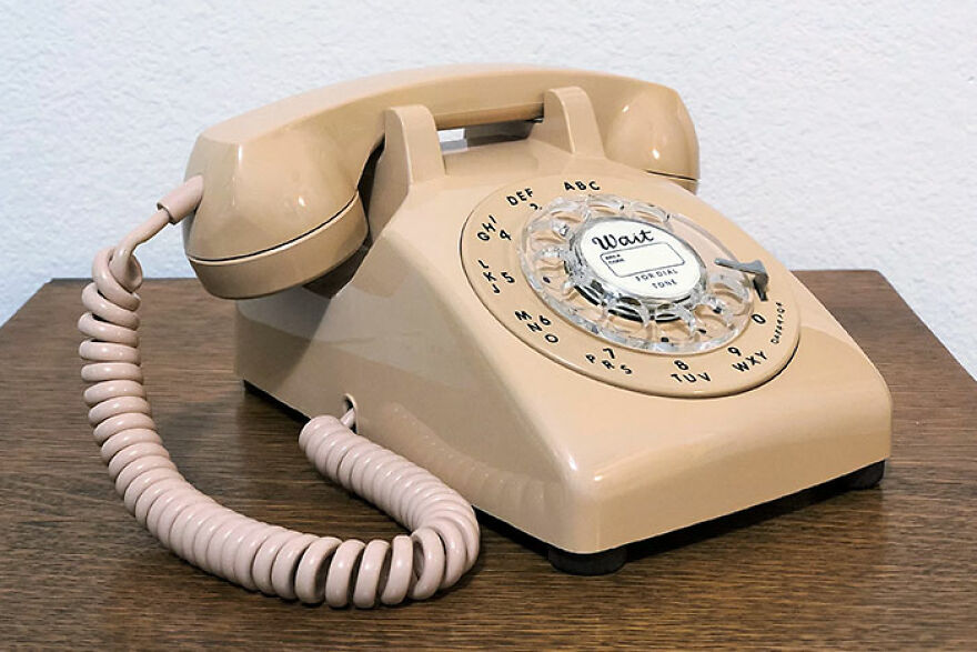 A beige rotary dial telephone with a coiled cord, sitting on a wooden table. This photo takes people down memory lane.