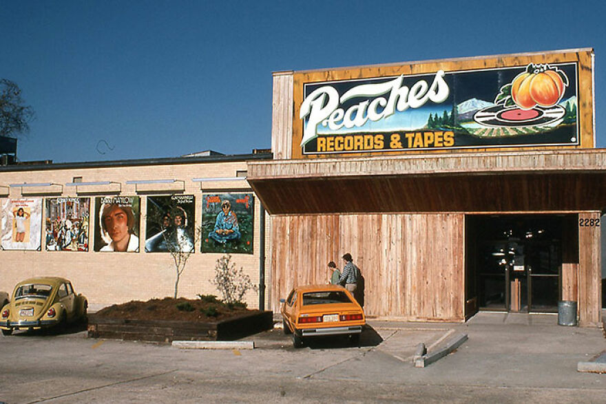 A vintage Peaches Records & Tapes store with large album covers, cars, and people, evoking a trip down memory lane.