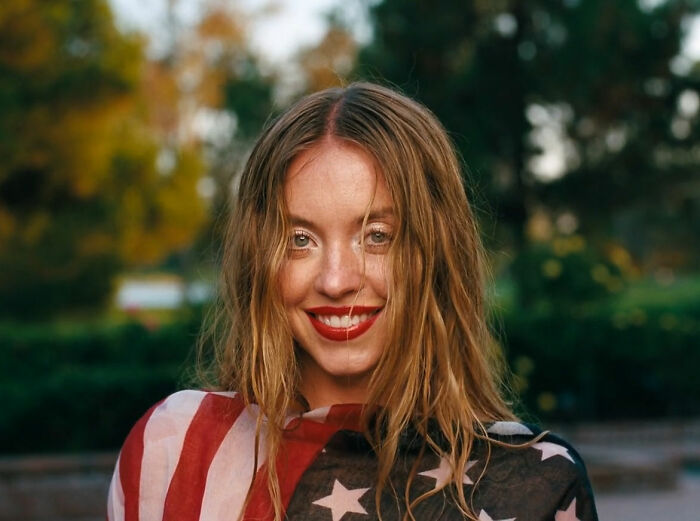 Sydney Sweeney smiling outdoors wearing an American flag patterned shawl, discussed in Euphoria backlash season 3 episode.
