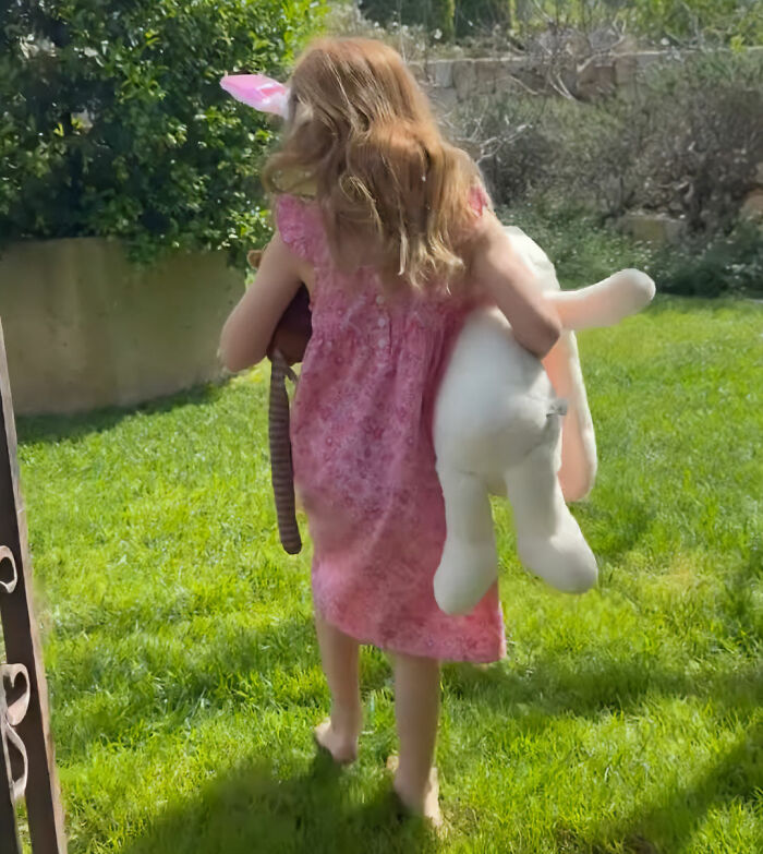 Young girl in pink dress carrying large stuffed bunny in grass, related to Meghan Markle Easter clip backlash detail.