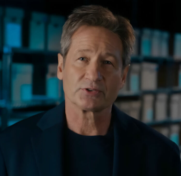 Estrela de TV dos anos 90 parecendo irreconhecível com uma peruca loira e saia enquanto sai durante as filmagens em ambientes fechados.