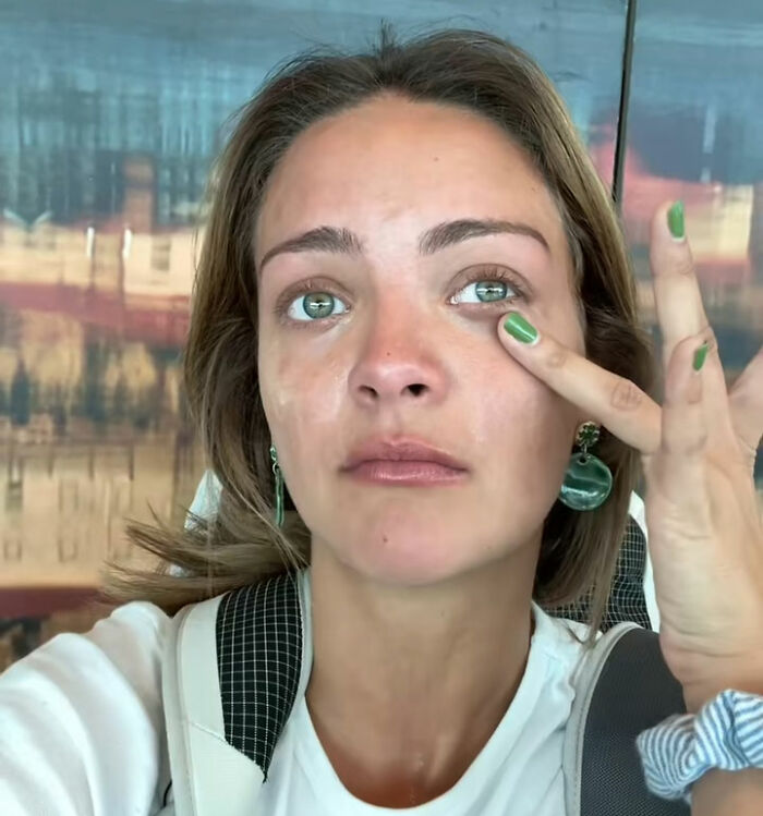 Young woman with green nails and earrings wiping tears, reflecting a health and wellness girly facing a brutal wake-up call after airline experience.