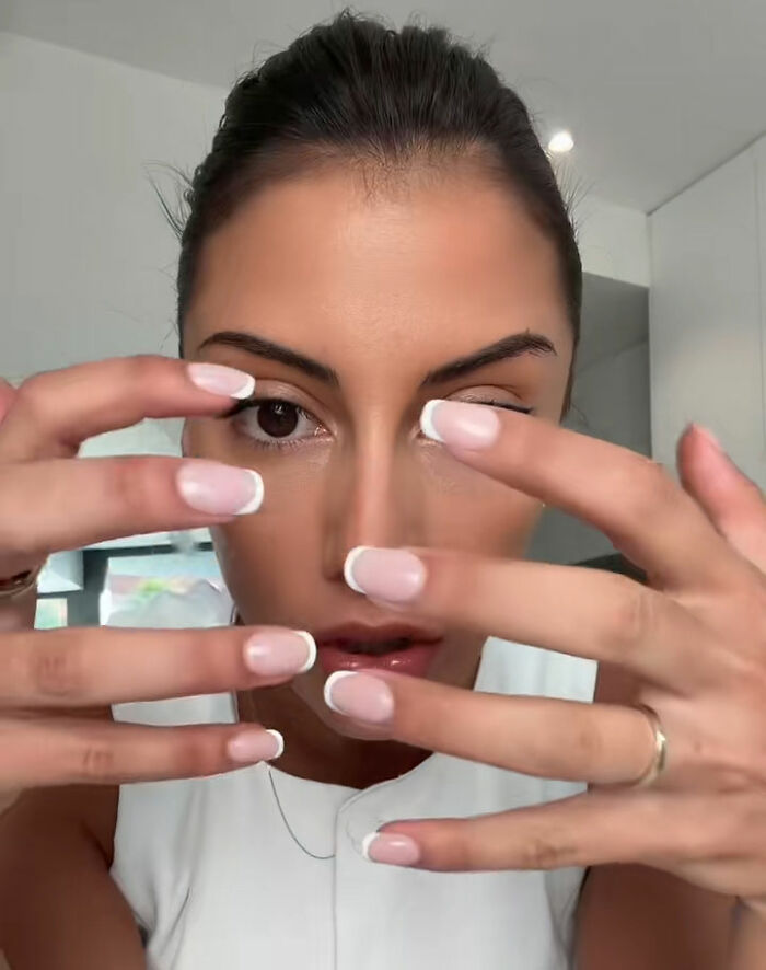Young woman showing French manicure nails as she issues urgent warning about going to nail salons and risks.