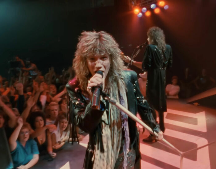 Lead singer performing on stage with band and energetic audience, highlighting amazing and interesting stories about moms.