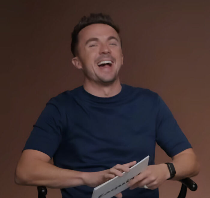 Man in a navy shirt laughing during an interview about Bryan Cranston’s brutal and direct remarks on Shia LaBeouf.