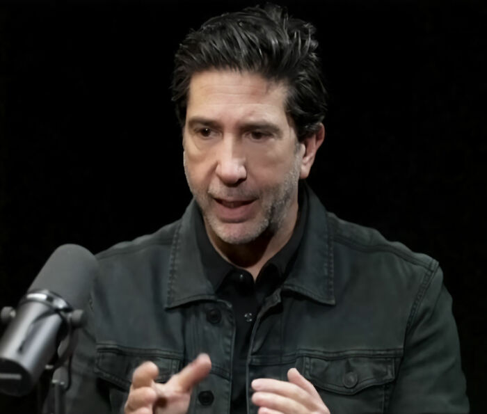 David Schwimmer falando ao microfone durante uma entrevista, abordando a controvérsia entre Kanye West e o Wireless Festival.