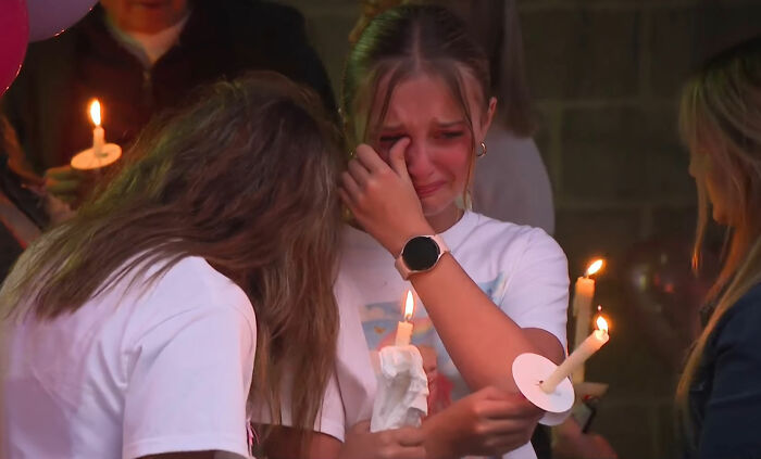 Uma jovem chora, enxugando os olhos, enquanto segura uma vela acesa em vigília pelo desaparecimento de uma criança de 9 anos.