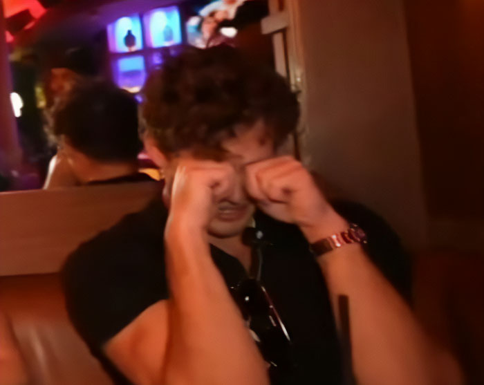 Looksmaxxer in distress covering face with hands in dimly lit room during livestream incident related to hospitalization.