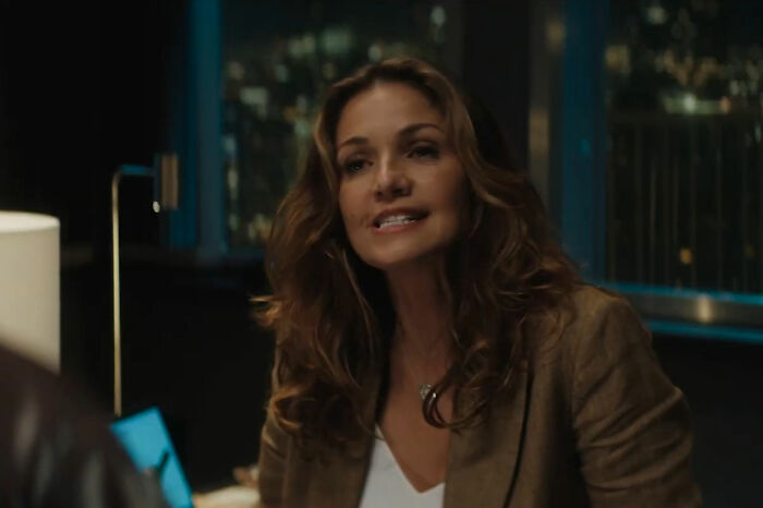 Mulher de cabelos castanhos ondulados, vestindo blazer, falando dentro de casa. Ela poderia ser o amor secreto de Mel Gibson, evitando acidentes na piscina?