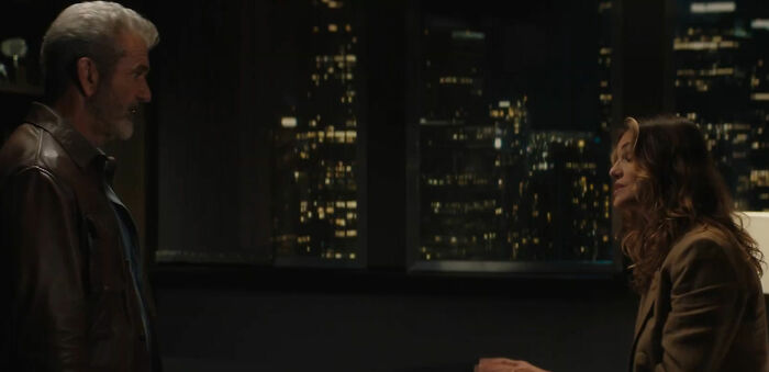 Um homem e uma mulher num apartamento à noite, paisagem urbana visível. A mulher lembra o amor secreto de Mel Gibson.