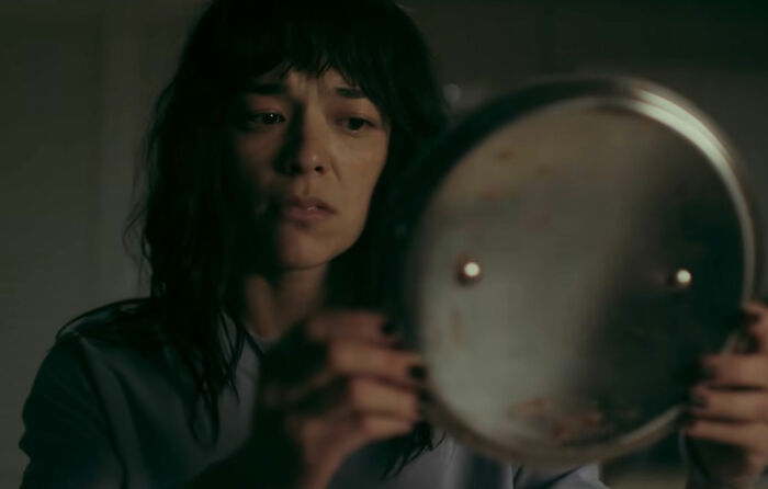 A woman with dark hair and bangs, looking worried while holding a pot lid, connecting to the horror movie about being thinner.