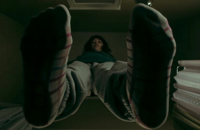 A terrifying close-up, low-angle shot of a person hanging, their striped socks and sweatpants visible, emphasizing the horror movie's theme of being thinner than ever.