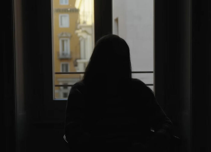 Silhouetted figure sitting in a dark room by a window, representing investigation into depraved website and crimes against wives.