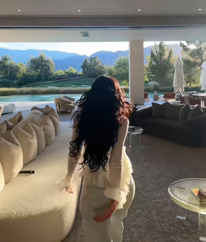 Pessoa caminhando pela luxuosa sala de estar moderna com vista para a piscina externa e as montanhas no tour da casa Coachella de Kylie Jenner.