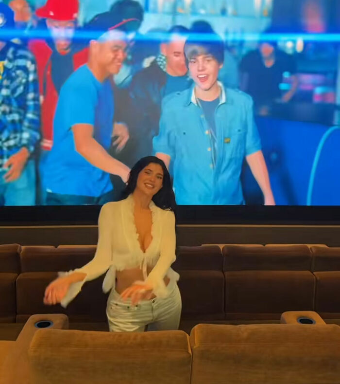 Mulher sorrindo em frente a uma tela grande em uma sala de teatro, relacionada à reação distópica da turnê da casa Coachella de Kylie Jenner.