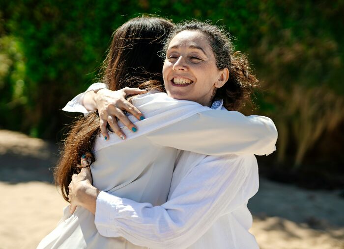 Two women smiling and hugging outdoors, showing normal family moments that seem bizarre in hindsight.