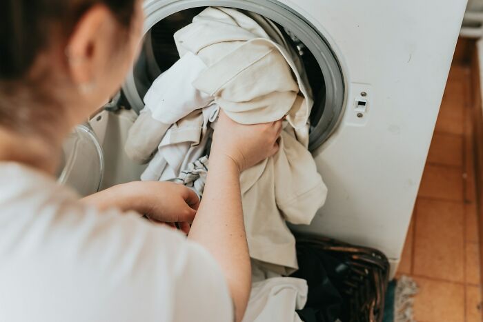 Person loading laundry into a washing machine, illustrating concepts of weaponized incompetence in daily chores.