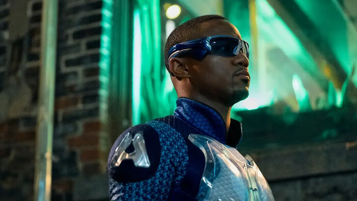 A-Train from The Boys in Season 5 wearing a blue suit and visor, standing in a dimly lit urban environment.