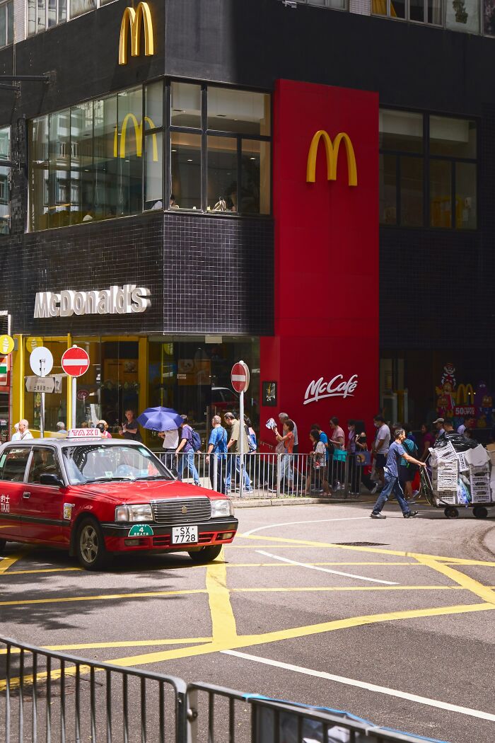 A busy Hong Kong street scene featuring a McDonald's, a red taxi, and people on the sidewalk. Some people rage quit their jobs for less stressful environments.