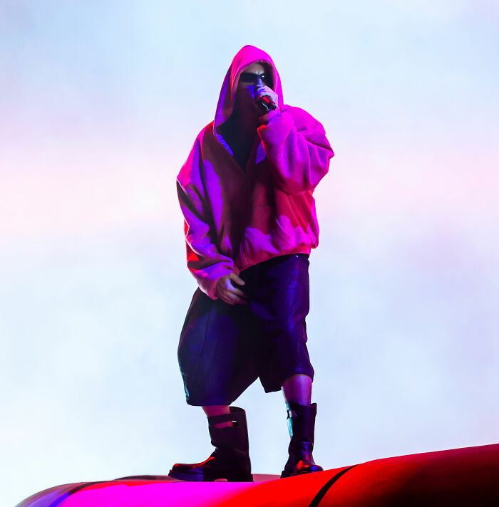 Performer in oversized red hoodie and black shorts with boots, highlighting absurd looks and fashion fails at Coachella 2026.