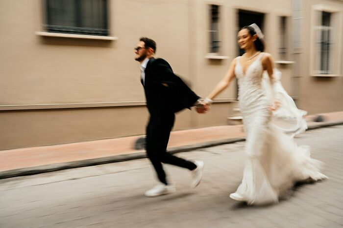 Bride in wedding dress and groom in suit running on street, illustrating how random life decisions lead people to right place.