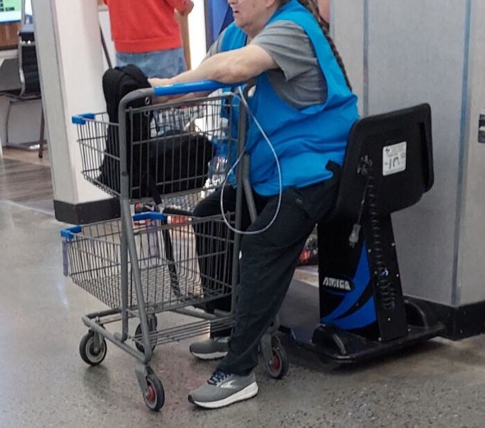 Woman in a blue vest using a motorized shopping cart and leaning on a cart in a store showcasing dystopian United States.